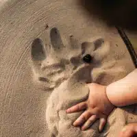 Enfant jouant dans le sable avec sa main.