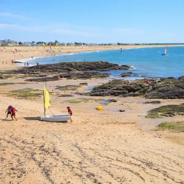 Plage ensoleillée avec voiliers et rochers.