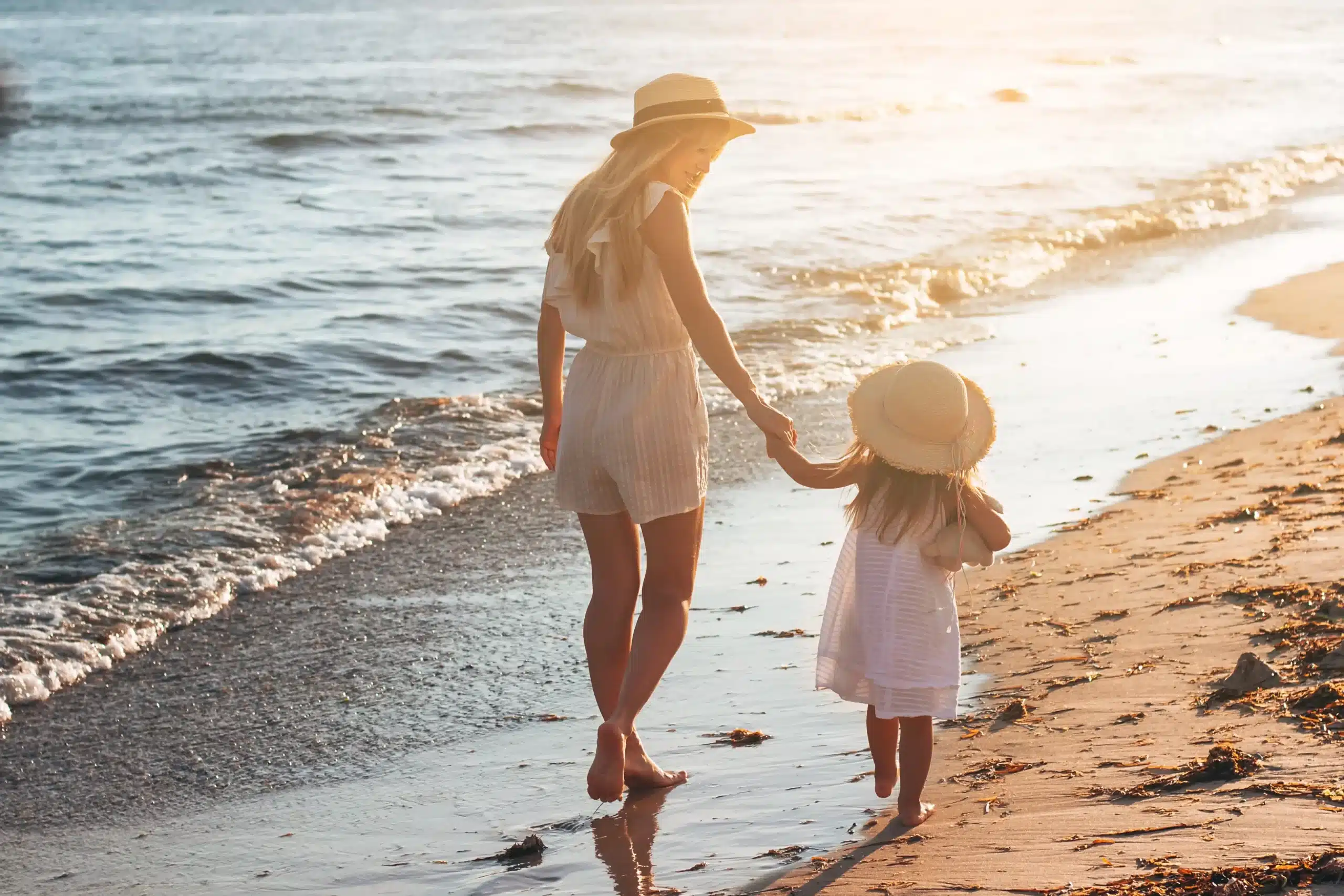 Mère et enfant marchant sur la plage au coucher du soleil.