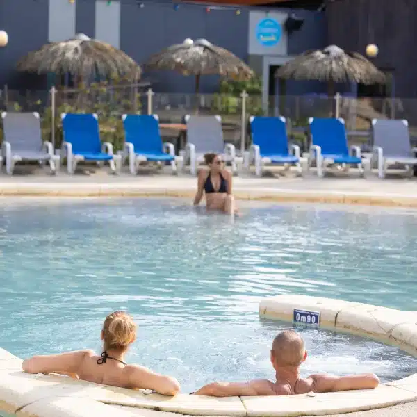 Personnes relaxant dans une piscine extérieure ensoleillée.