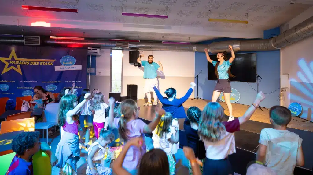 Enfants dansent avec animateurs sur scène.