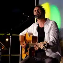 Homme chantant avec une guitare sur scène.